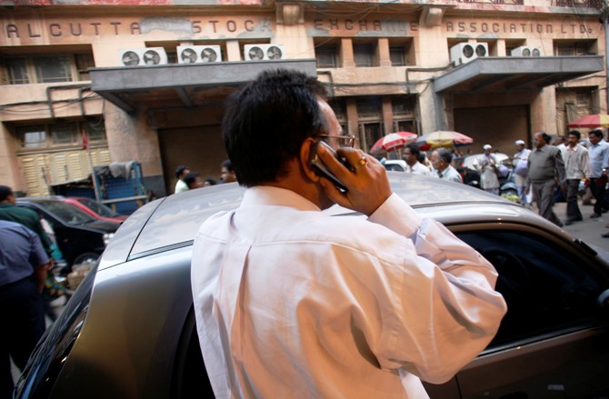 An investor monitors stock news through a mobile phone in front of the Kolkata Stock Exchange building.