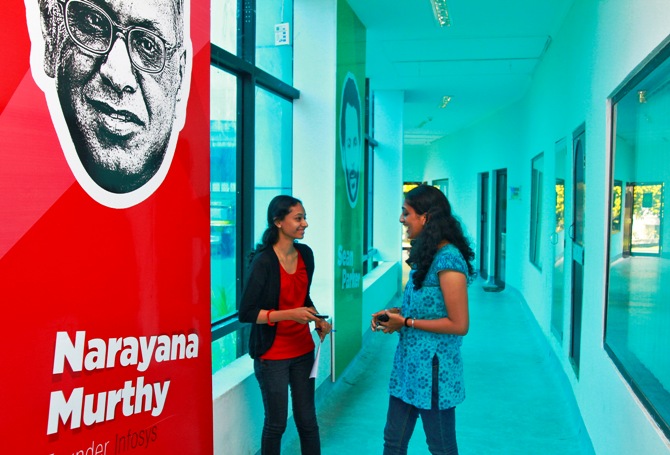 Employees talk as they stand next to flex board poster of Infosys founder Narayana Murthy at the Start-up Village in Kinfra High Tech Park in Kochi.