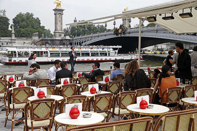 People sit at a terrace cafe near the Alexandre III bridge between the Orsay Museum and Alma Bridge on the left bank of the River Seine in Paris, France.