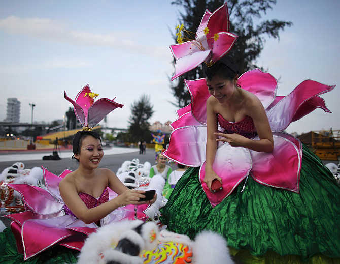 A performer poses in front of a Chinese lion head as her friend takes photo before the dress rehearsal for the Chingay parade in Singapore.