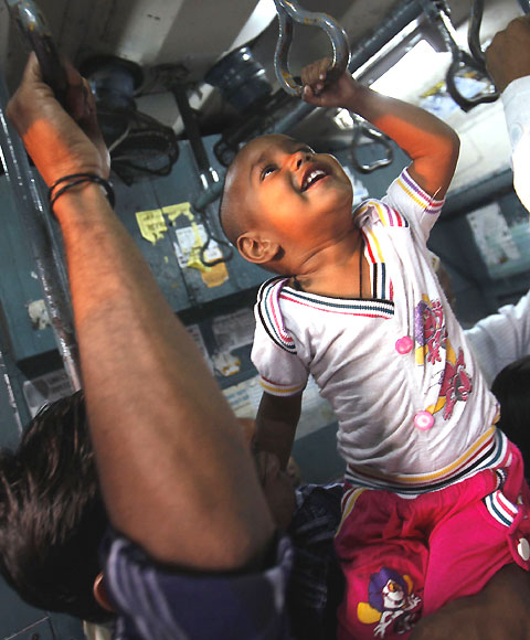 A child tries to hold onto the handrails in a crowded suburban train.
