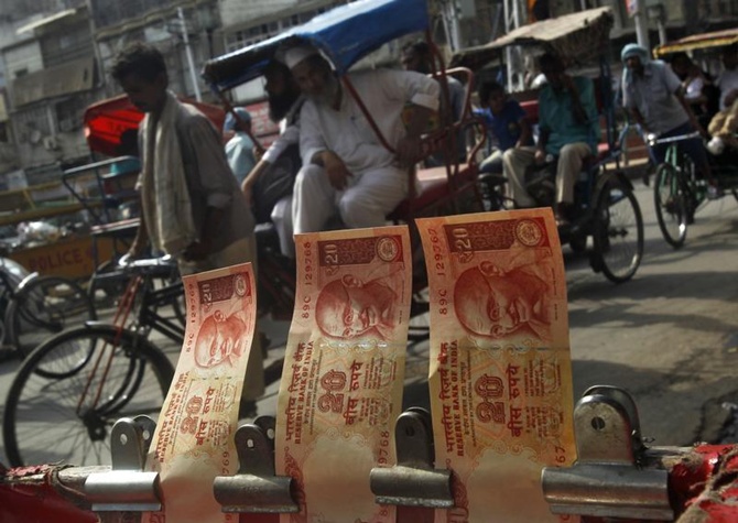 Cycle rickshaws move past a display of rupee notes at a roadside currency exchange stall in Delhi.