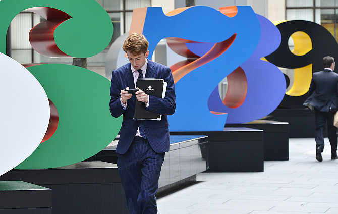A worker uses his mobile phone as he walks past sculptures in the City of London.