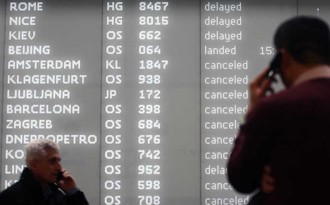 Men talk on their mobile phones while standing in front of an electronic information board at Vienna airport, Austria.