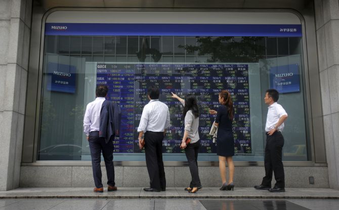 Pedestrians stand in front of a stock quotation board displaying various stock prices outside a brokerage in Tokyo.