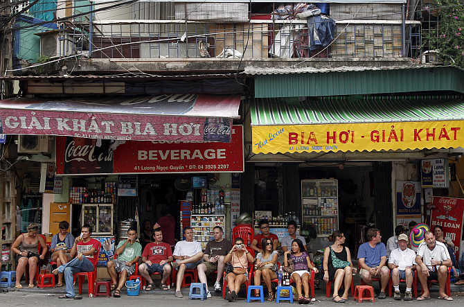 Tourists sit on stools and drink beer outside a beverage shop along a street at the old quarters in Hanoi, Vietnam.