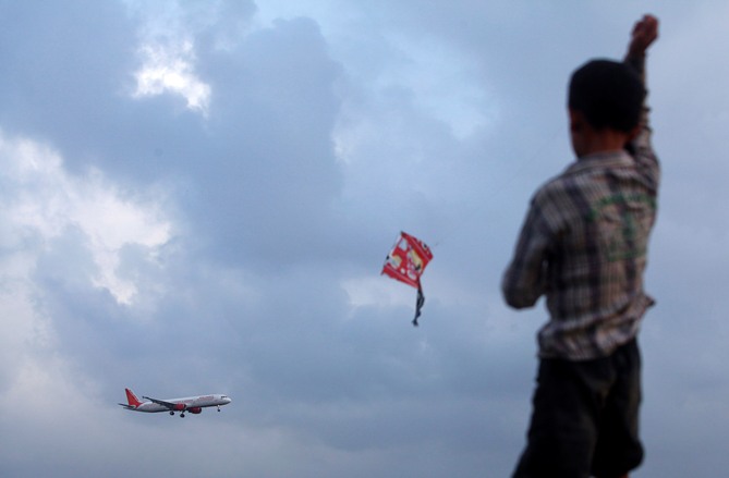 A boy flies a kite from a rooftop overlooking Chhatrapati Shivaji International Airport, as a Boeing 737 aircraft belonging to Air India comes in to land in Mumbai.