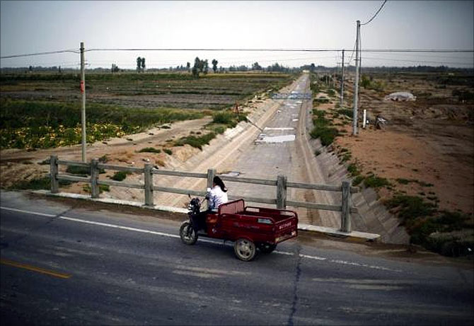 A farmer drives an electric tricycle across an irrigation canal near the dried up Shiyang river on the outskirts of Minqin town, Gansu province.