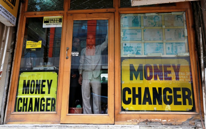 Two men look out from the glass door of a currency exchange shop in New Delhi.