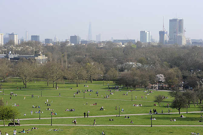 People sit in the sunshine on Primrose Hill in north London, United Kingdom.