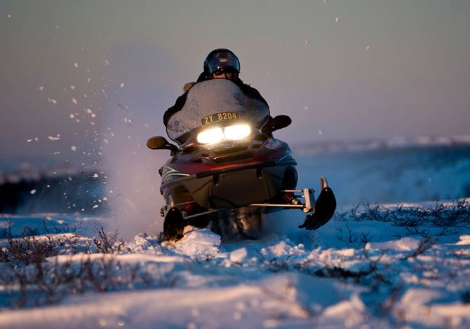 Guest ride a Snowmobile at the Sorrisniva Igloo Hotel.