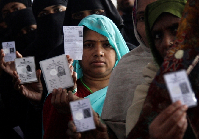 Voters display their voter identity cards as they wait for their turn to cast their ballot at a polling station.