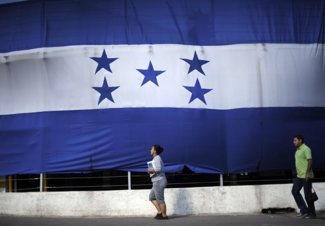 A woman and a man walk past a giant Honduran flag in Tegucigalpa.