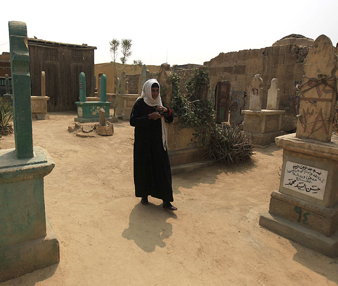 A woman walks near tombs in front of her home.