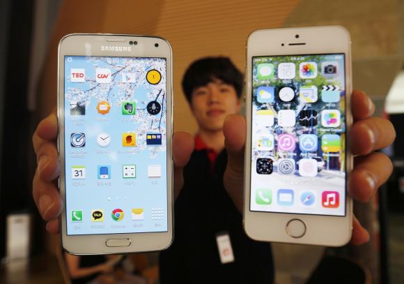 A sales assistant holding Samsung Electronics' Galaxy 5 smartphone (L) and Apple Inc's iPhone 5 smartphone (R) poses for photographs at a store in Seoul July 16, 2014. 