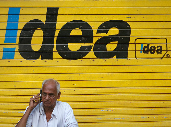 A man speaks on his mobile phone as he sits in front of a shop displaying the Idea Cellular Ltd's logo on its shutter in Mumbai.