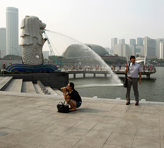 Tourists take photos of the Merlion in the hazy skyline of Singapore.