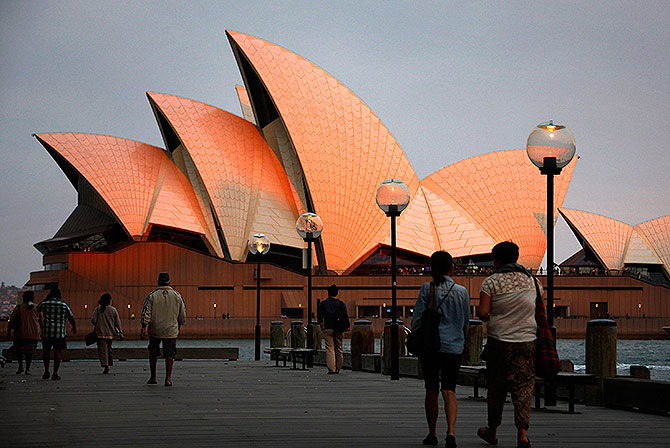 People look at the Sydney Opera House as they walk past at sunset.