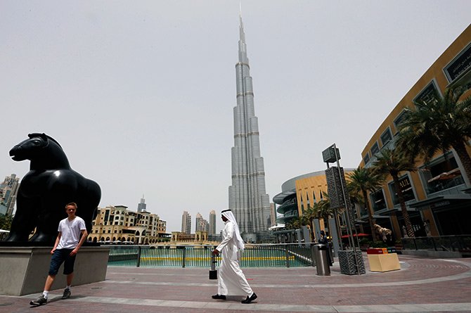 An Emirati man walks past a tourist posing for a photo near the Burj Khalifa, the tallest tower in the world, in Dubai.