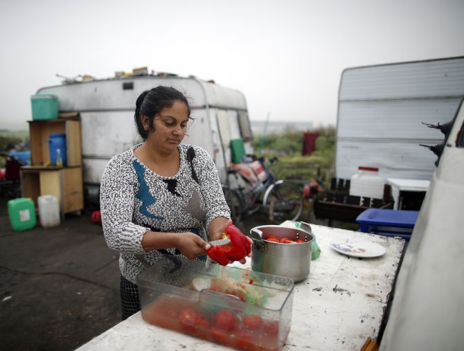 A Roma woman cooks vegetables in front of caravans at an encampment of Roma families near Paris.