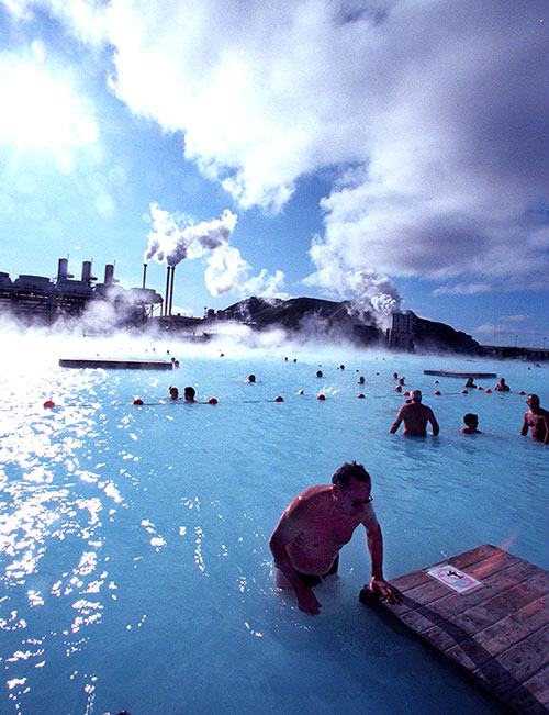 Bathers at the Blue Lagoon hot springs swim in hot mineral waters amid a chilly wind as a thermal electricity plant looms in the background.