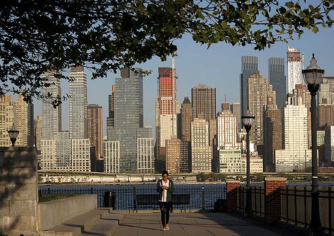 A woman walks along a promenade next to the Hudson River across from the skyline of New York in Weehawken, New Jersey.