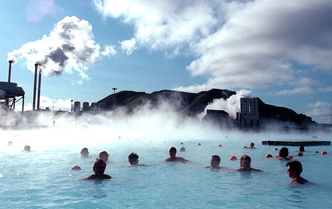 Bathers at the Blue Lagoon hot springs swim in hot mineral waters amid a chilly wind as a thermal electricity plant looms in the background.