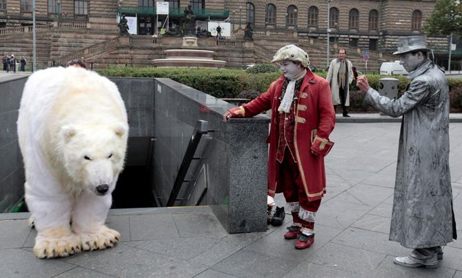 Street performers look at Greenpeace environmental activists dressed up as a polar bear in Prague October 13, 2014. 