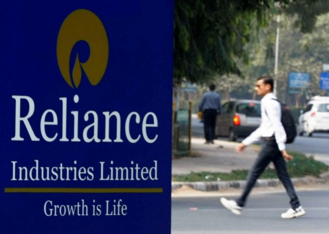 A man walks past a Reliance Industries Limited sign board installed on a road divider in Gandhinagar.