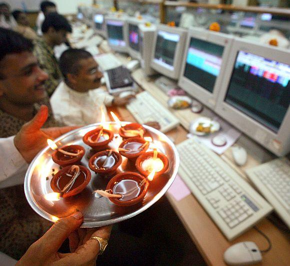 A Hindu priest holds traditional earthen lamps in front of computers while offering prayers during 'Muhurat' trading. 