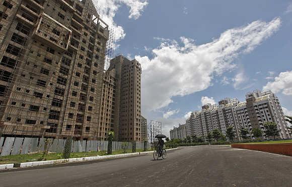 A man holds an umbrella while cycling past residential buildings under construction in Kolkata.