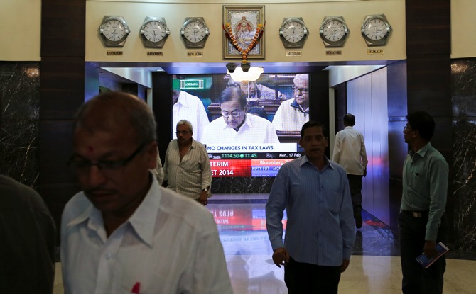 People walk in the lobby as a telecast of Finance Minister P Chidambaram presenting the interim budget is displayed inside the Bombay Stock Exchange building in Mumbai February 17, 2014.