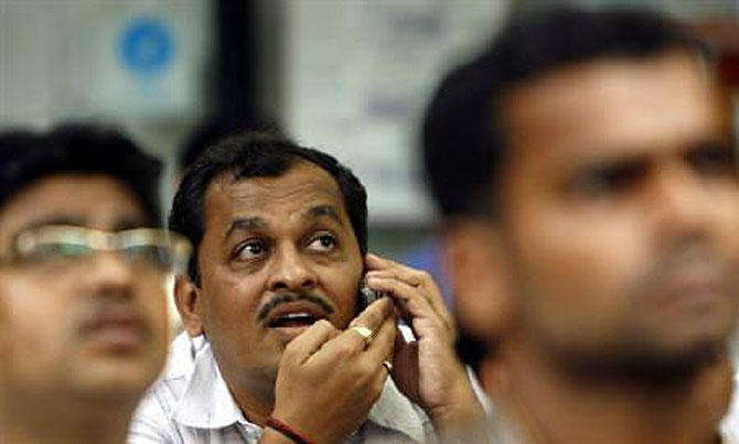 A man speaks on a mobile phone as he looks at a large screen displaying share index on the facade of the Bombay Stock Exchange.