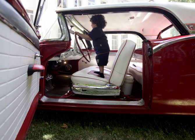A child plays at the wheel of a 1957 Ford car.
