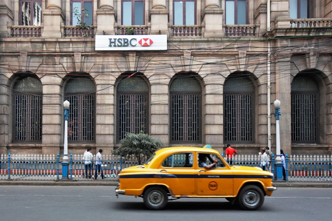 A yellow ambassador taxi drives past the HSBC bank building in Kolkata.