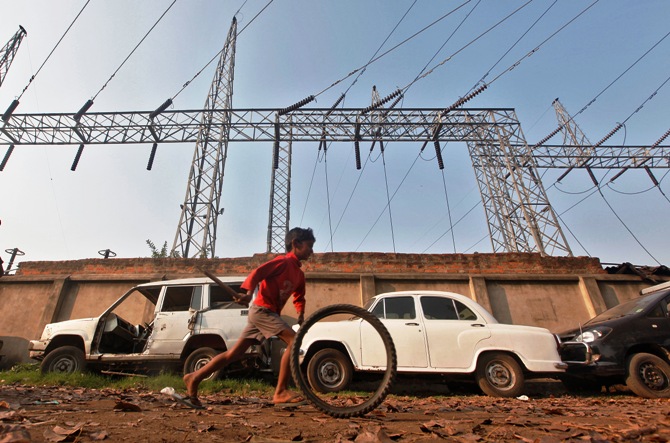 A boy plays with a tyre in front of electric pylons installed at a power house in Kolkata.