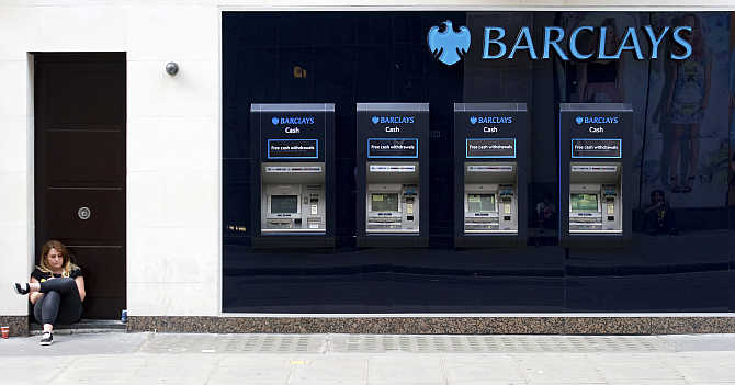 A woman sits close to a line of Barclays cash dispensers in central London.
