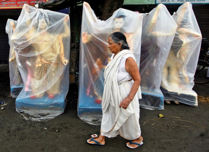 A woman walks past the plastic wrapped idols of Vishwakarma, the Hindu deity of architecture and machinery, kept on display for sale at a roadside in Kolkata.