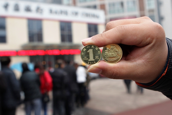 A resident displays newly-issued one Chinese yuan souvenir coins, to commemorate the Year of the Horse, as people queue to exchange the coins outside a Bank of China branch in Neijiang, Sichuan province December 24, 2013.