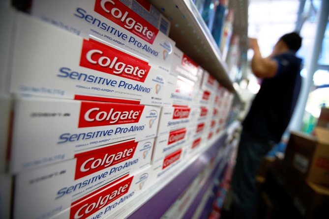A worker arranges Colgate products on a shelf at a supermarket.
