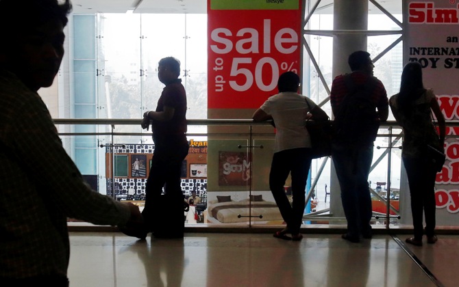 Shoppers are silhouetted as they stand near a sign advertising a sale at a shopping mall in Mumbai.