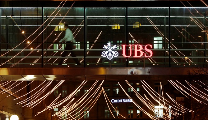 A man walks past the logo of Swiss Bank UBS on a footbridge connecting two office buildings in Zurich.