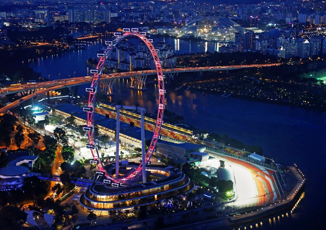 An aerial view shows the main grand stand and the Formula One pit building behind the Singapore Flyer observation wheel at dusk.