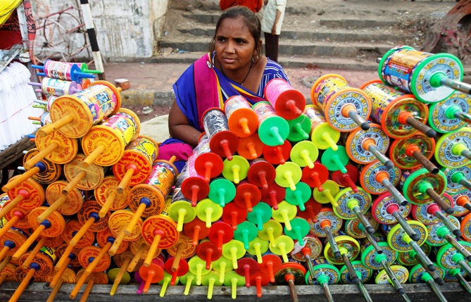 A vendor sits at her stall selling reels of thread used to fly kites, at a roadside kite market.