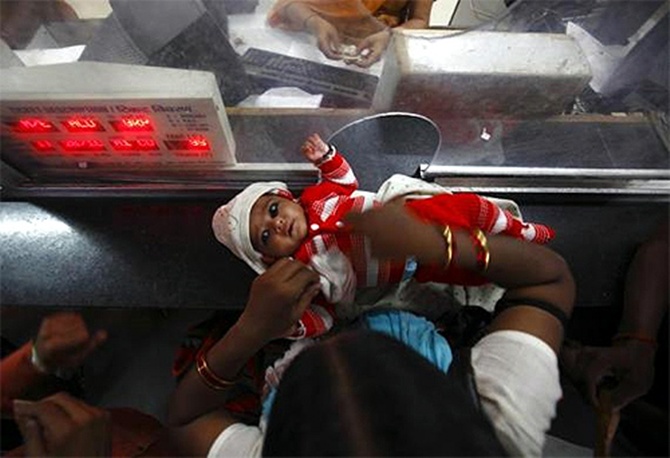 A woman keeps her child on the ticket counter as she buys a train ticket.
