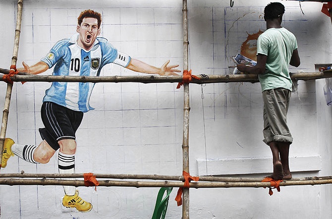 An artisan paints a roadside wall with pictures of 2014 World Cup participating players, in Kolkata.