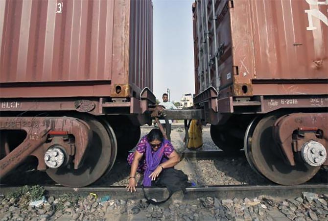 A woman crosses under the carriages of a parked goods train at Loni town in Uttar Pradesh.