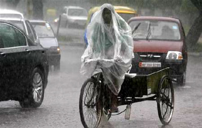A man uses a plastic sheet to guard against a downpour while riding his trishaw in Chandigarh.