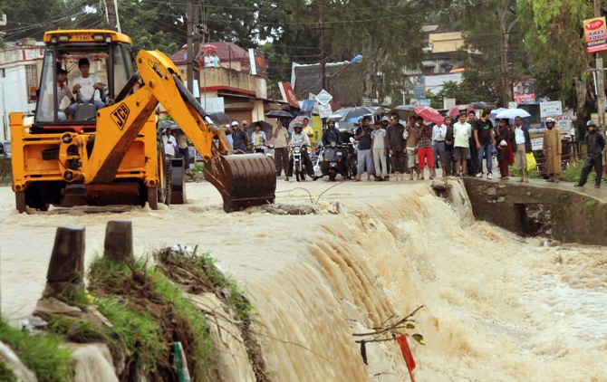 A bulldozer removes waste floating on a flooded street in Dehradun.