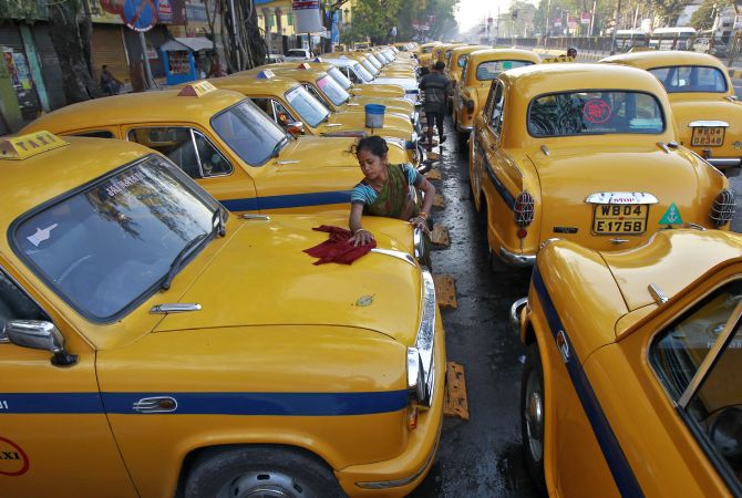 Sumitra Sarkar, 35, cleans a yellow ambassador taxi at a parking area along a roadside in Kolkata.